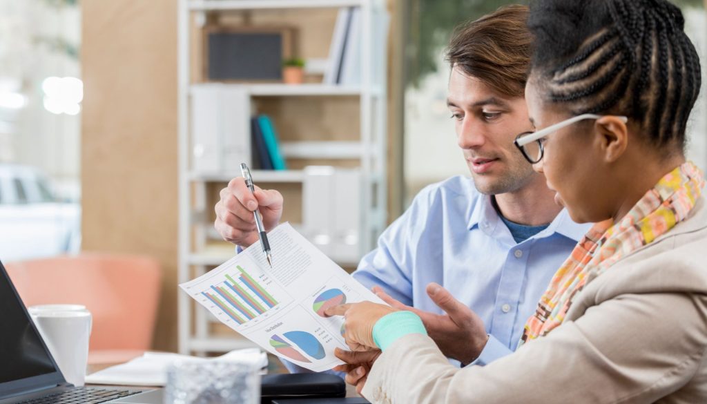 two business people review charts and graphs together in an office.