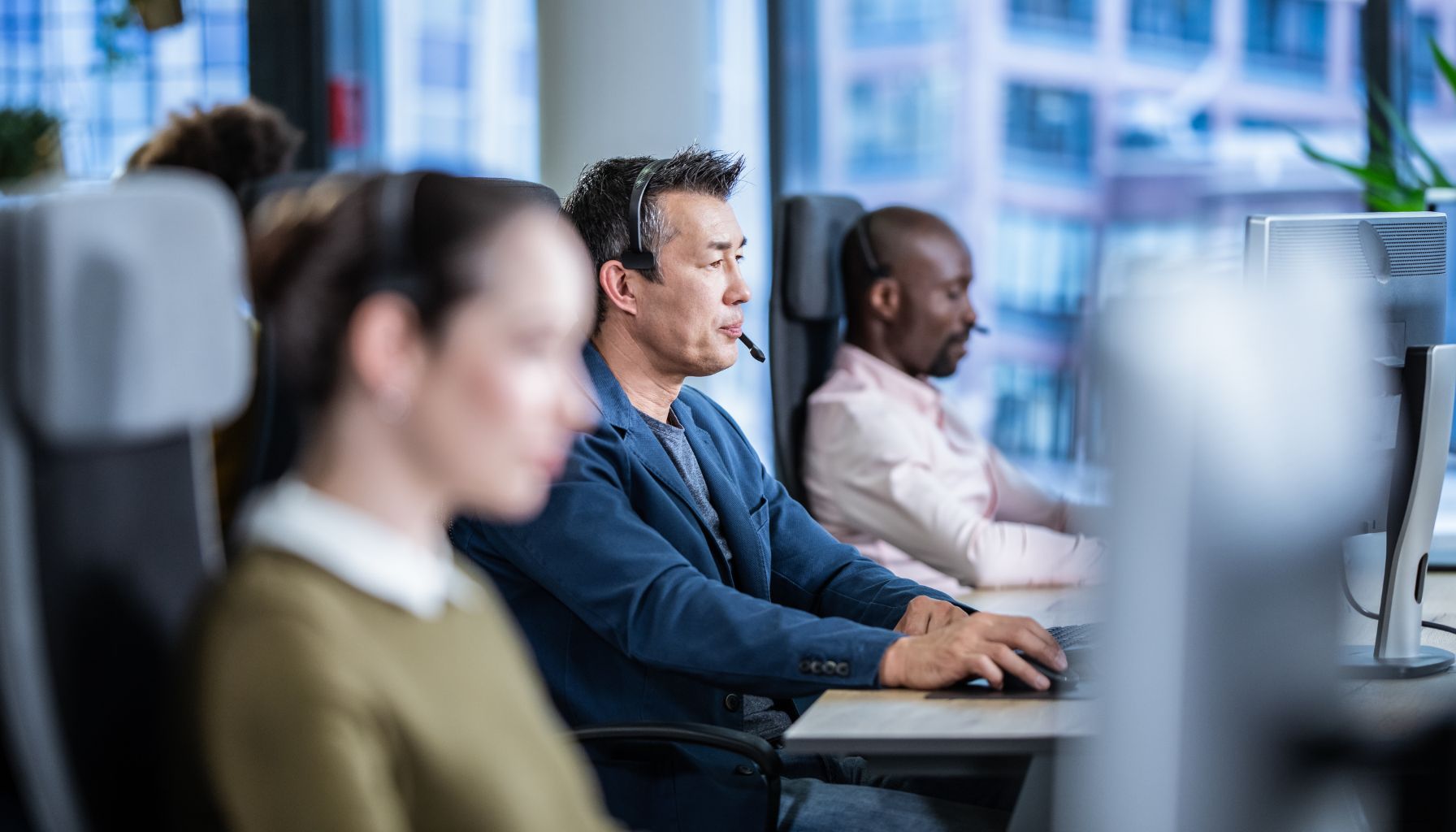 people in call center sitting behind desks using computers and talking to customers over headsets while conducting market research